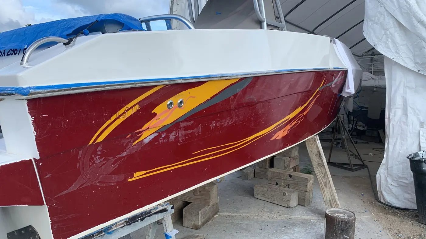 Old faded graphics on a red hull before refinishing by SXM Refinishing in St. Maarten